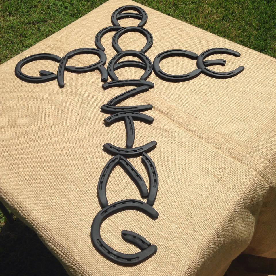 Decorative cross made from horseshoes on a beige surface with grass in the background