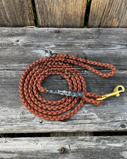 Brown braided dog leash with brass clip on a wooden surface, branded 'Lucky U Custom Designs'.
